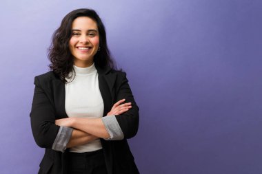 İspanyol iş kadını kendine güvenerek gülümsüyor. Stüdyoda mor geçmişiyle kollarını kavuşturuyor. Başarı ve liderliği temsil ediyor.