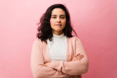 Kolları çapraz duran, dudağını ısıran düşünceli bir kadın. Pembe bir zeminde kendine güvenen ve karar veren bir kadın.