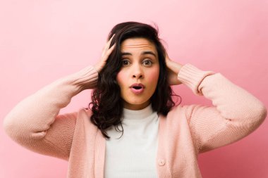 Şaşkınlık gösteren genç bir kadın, gözleri açık ve ağzı o şeklinde, hayret verici haberlere tepki veriyor ya da pembe duvara karşı ani bir olay.