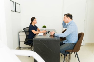 Male patient showing an area of his head to a female doctor, discussing symptoms of hair loss and receiving advice from the specialist