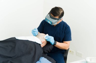 Doktor saç nakli yapıyor. Özel tıbbi aletlerle hastanın kafa derisine folikülleri dikkatlice yerleştiriyor.