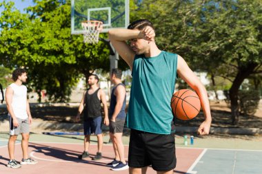 Aktif bir adam alnından ter siliyor, dışarıda arkadaşlarıyla basketbol oynadıktan sonra yorgun hissediyor.