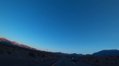 Gün batımında bir araba Birleşik Devletler 'deki dağlık araziden geçiyor..