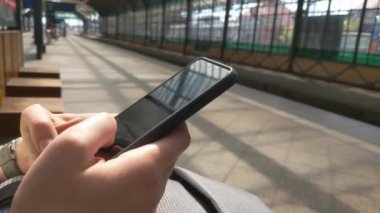 Kız istasyonda bir bankta oturmuş treni bekliyor. Telefona bakar, sayfaları yapıştırır.