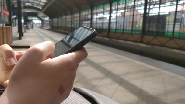 Κορίτσι Κάθεται Ένα Παγκάκι Στο Σταθμό Περιμένοντας Τρένο Κοιτάζει Τηλέφωνο — Αρχείο Βίντεο