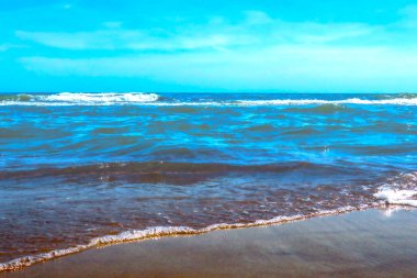Güneşli bir günde denizin turkuaz sularının resimli görüntüsü. Dalgalar kıyıya vuruyor. Kumsalda dinlen.