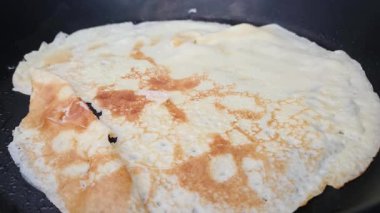 A close-up view of a homemade crepe cooking in a frying pan. the crepes golden-brown texture contrasts with lighter areas, perfect cooking. ideal for culinary blogs, cooking tutorials, or breakfast-themed designs.