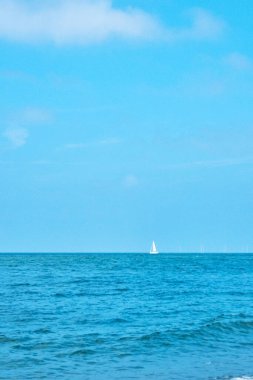 Calm ocean waters stretch to the horizon under a clear blue sky, with a solitary sailboat in the distance creating a serene and peaceful ambiance. ideal for travel, relaxation, and maritime-themed projects.
