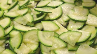 Taze dilimlenmiş kabak parçaları, canlı yeşil renklerini ve nemli dokularını sergiliyor. Taze malzeme ve besinleri vurgulayan sağlıklı yemek tarifleri, salatalar ve mutfak sunumları için mükemmel..