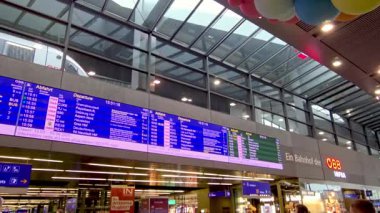 Viyana, Avusturya, 5 Mayıs 2025: Modern bir tren istasyonu tren saatlerini gösteren büyük bir dijital kalkış panosuna sahiptir. Çağdaş mimari sergilenen cam panelli yüksek tavanlar. Bilgiler birden fazla dilde,