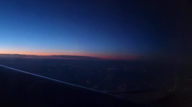 Alacakaranlık çökerken nefes kesici bir hava manzarası, günden geceye canlı geçişi gösteriyor. Uçak kanadı, şehir ışıklarının altta yanıp söndüğü ve yukarıda parlak bir ufuk oluşturduğu uçuş yolculuğunun deneyimini vurgular..