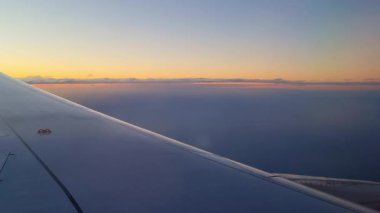 Ufukta canlı bir günbatımını gösteren bir uçak penceresinden çarpıcı bir hava görüntüsü. Kanat, dingin manzaraya derinlik katıyor. Gezginler için merak ve gezginlik hissi uyandırıyor..