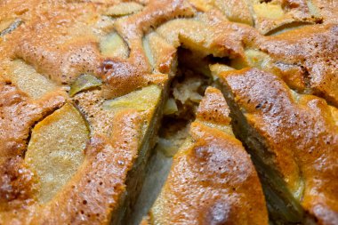 Yeni ev yapımı, kahverengi kabuklu ve görünür elma dilimli bir elmalı kekin yakın çekimi. Pasta kısmen dilimlenmiş, içi nemli. Sonbahar, tatil ya da sıcak aile toplantıları için mükemmel..