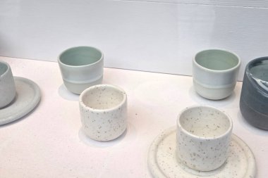 Beyaz bir yüzeyde seramik fincan ve fincan tabakları sergileniyor. Bu parçalar, yumuşak, sessiz renkleri ve benekli desenleri olan, çağdaş ev dekorasyonu ve iç dekorasyon için mükemmel minimalist bir tasarıma sahiptir..