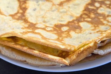 Tabağa istiflenmiş altın kahverengi kreplerin yakın plan görüntüsü çıtır çıtır kenarlarını ve hassas dokusunu gözler önüne seriyor. Kahvaltıyla ilgili görseller, yemek blogları ya da geleneksel yemek tarifleri için mükemmel..