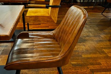 Samimi bir kafe ortamında eski bir deri koltuğun yakın çekim görüntüsü. Derinin zengin kahverengi tonları, sıcak ahşap döşemeleri tamamlar, kırsal iç tasarım için mükemmel davetkar ve şık bir atmosfer yaratır..