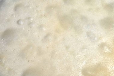 Köpüklü köpüklü bir yüzeyin yakından görüntüsü kabarcıklı, desenli bir desen sergiliyor. Doğal ve yumuşak estetik arayışında kullanım için ideal arka plan, grafik tasarım veya yaratıcı projeler. resim değişik kabarcık boyutlarını ve kremsi bir tonu vurgular.
