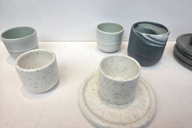Minimalist seramik bardaklar ve bardaklar beyaz bir yüzeyde gösterilir, benekli ve pürüzsüz bir şekilde bitirilir. Tasarım basitliği ve zarafeti vurgular, çağdaş yemek estetiği için mükemmeldir..