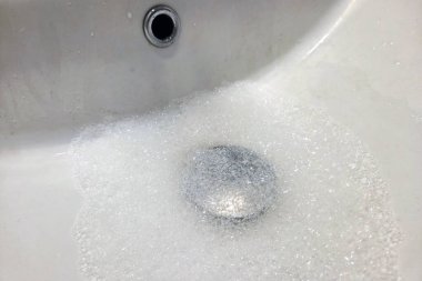 Sabun köpüğü dolu bir lavabo, ev temizliği ve hijyen. Olay yeri, evlerde dikkatli su yönetimi ve temizliğe duyulan ihtiyacı vurgulayan tesisat bakım sorunlarını temsil ediyor..
