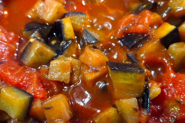 Canlı, baharatlı bir sosun içine yerleştirilmiş patlıcan ve domates küplerinin yer aldığı zengin renkli bir ratatouille çanağının yakın plan görüntüsü. Dokular ve renkler bu klasik provenkal tarifin rustik cazibesini ve aromatik cazibesini vurgular..