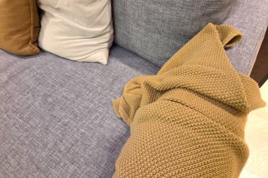 Yumuşak gri bir kanepe kumaştan örülmüş bir battaniye ve bej ve kahverengi tonlarında peluş yastıklarla süslenmiş. Sahne bir sıcaklık ve rahatlama hissi uyandırıyor, oturma odası tasarımı ve ev konsepti için mükemmel..