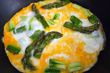 Taze kuşkonmaz tavada pişerken omleti tamamlar, sarı ve yeşil renkli canlı bir karışım sergiler. Bu gurme kahvaltısı basit ama zarif bir sunumla sağlıklı beslenmeyi ön plana çıkarıyor..