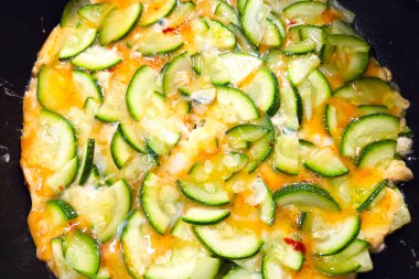 Taze kabak dilimleri, erimiş peynir ve bitkilerle pişirilmiş renkli bir kabak omleti. Yemek, hem iştah açıcı hem de sağlıklı besleyici bir yemek seçeneği sunan mükemmel bir doku ve lezzet karışımını ön plana çıkarıyor..