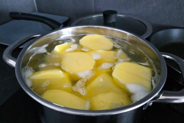 Dilimlenmiş patatesler fırının üstünde paslanmaz çelik bir tencerede kaynayan suyla kaynıyor. Sahne, ev yemeği pişirme, yemek hazırlama ve mutfak ortamlarında basitlik hissi veriyor..