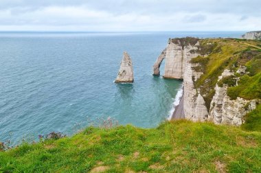 Fransa 'daki ikonik uçurumların ve etretatın doğal kemerinin yer aldığı kıyı manzarası. Sahne, yemyeşil çimenler ve uçsuz bucaksız mavi deniz arasındaki zıtlığı vurguluyor. Bu da doğal güzelliğin ve coğrafi harikanın bir örneği..