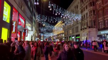 Londra, İngiltere, 13 Aralık 2025: Şenlikli ışıklar ve dekorasyonlarla süslenmiş hareketli bir akşam sokak sahnesi. Büyük bir kalabalık dükkanların ve aydınlatılmış binaların hareketli atmosferinin tadını çıkarıyor. Şehir tatili heyecanı ve kutlamaları iletmek için mükemmel..