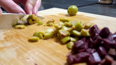 Taze yeşil ve siyah zeytinler ahşap bir kesim tahtasına dilimleniyor, aşçılık hazırlığı süreci. detaylı bir yakın çekim görüntü dokusu ve renkleri, yemek tarifleri veya mutfakla ilgili tasarımlar için mükemmel.