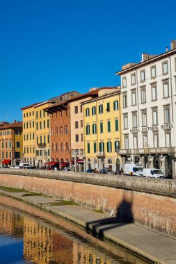 Pisa, İtalya, 27 Aralık 2025: İtalya 'nın pisa kentindeki Arno Nehri' ni çevreleyen bir dizi renkli tarihi bina sergilenmektedir. Sıcak güneş ışığı, suya güzel bir şekilde yansıyan çeşitli mimari ve canlı cepheleri vurgular..