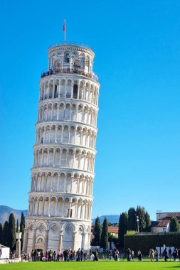 Pisa, İtalya, 27 Aralık 2025: Sidikli kule, ziyaretçiler ve yemyeşil ile çevrili açık mavi gökyüzüne karşı görkemli bir şekilde duruyor. Bu mimari harikası Rönesans mühendisliği dünyanın dört bir yanından turistleri kendine çekiyor..