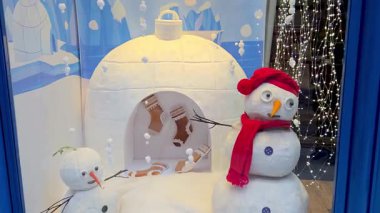 Bolonya, İtalya, 3 Ocak 2026: Parlak kırmızı aksesuarlar, rahat bir igloo ve içinde asılı çoraplarla süslenmiş bir kardan adamın yer aldığı şenlikli bir kış vitrini. Kartaneleri ve parıldayan ışıklarla çevrili bir tatil ortamı yaratıyor..