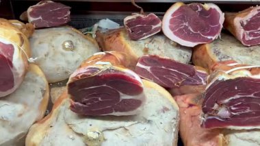 Bir şarküteri tezgahında, belirgin bir şekilde bütün ve dilimlenmiş prosciutto sergilenen çeşitli pişirilmiş etler bulunur. Zengin mermerler ve dokular sanatsal kaliteyi vurguluyor, gurme meraklılarına ve aşçılık uzmanlarına çekici geliyor..