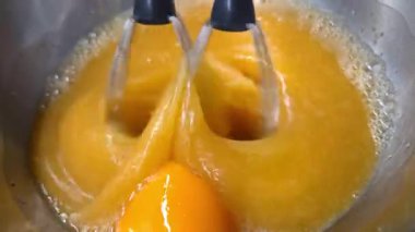 Yumurta sarılarını karıştıran iki çırpıcının yakın çekim görüntüsü, dinamik hareket ve doku. Yemek pişirme, pişirme ve aşçılık teknikleri için ideal. Yemek hazırlama temaları ve tarif sunumları için mükemmel görsel.