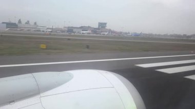 Bologna, İtalya, 4 Ocak 2026: Uçak motoru havaalanı operasyonları arasında piste yaklaşıyor. Terminal ve arka planda birden fazla uçak görünüyor. Bulutlu gökyüzü, hareketli havaalanının üzerine bastırılmış bir ışık salıyor..