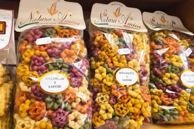 Bolonya, İtalya, 3 Ocak 2026: Bir mağaza rafında renkli makarna paketleri gösteriliyor. Her çanta farklı şekiller ve renkler içeriyor. Ekranda doğal malzemelerle yapılan makarnanın çeşitliliği vurgulanıyor.