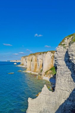 Dalgalı mavi bir deniz ve berrak bir gökyüzüne karşı yükselen kıyı kayalıklarının nefes kesici manzarası. Sahne şaşırtıcı doğal kaya oluşumları ve sakin okyanus dalgaları yavaşça kıyıya vuruyor..