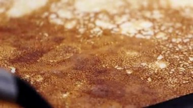 Tavada pişen bir gözlemenin yakın plan görüntüsü, altın-kahverengi dokusunu ve baloncuklarını vurguluyor, mutfakta çevirmeye hazır bir spatula ile