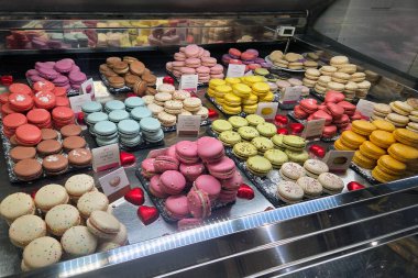 Floransa, İtalya, 1 Ocak 2026: Cam bir vitrinde çeşitli aromalar ve dolgularla çeşitli renklerde makarna dizileri. Hamur işlerinin canlı renkleri ve hassas dokuları dekoratif kırmızı kalp süslemeleriyle vurgulanır..