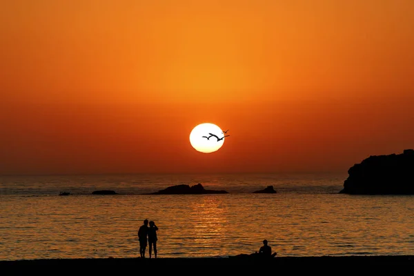 Sahilde insanlarla okyanusun üzerinde renkli bir gün batımı.