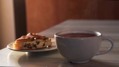 Beyaz fincana sıcak siyah çay dökmek. Bardaktan buhar çıkıyor. Turta arka planında.