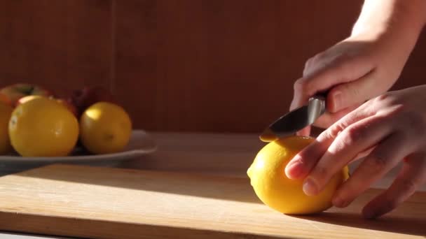 Kvinnliga händer skivning med kniv en citron på träbord i köket på en solig dag. — Stockvideo