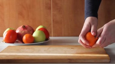 Güneşli bir günde mutfakta, ahşap masada mandalina soyan kadın elleri..