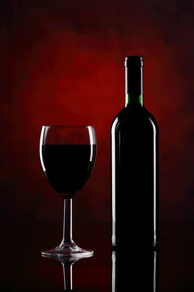 Copa de vino tinto con botella en el fondo rojo — Foto de Stock