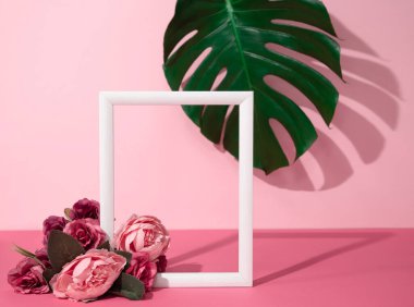 Arkaplanda çiçekler ve canavar yaprağıyla süslenmiş boş ahşap çerçeveli yaratıcı kadınsı bir düzen. Romantik ya da sevgililer günü temalı modaya uygun pembe bir model.