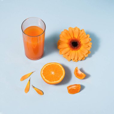Mavi arkaplana karşı turuncu renkli nesneler. Mandalina yarısı, papatya çiçeği, bir bardak meyve suyu. Yaz, rahatlama, ferahlatıcı konsept. 