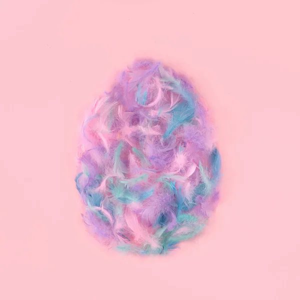 Easter egg shape made of colorful fluffy feathers on pink background. Minimal spring or Easter concept, flat lay pattern.