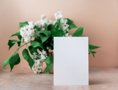 Masanın üzerinde duran boş beyaz kağıt not. Arka planda taze çiçek süslemesi var.